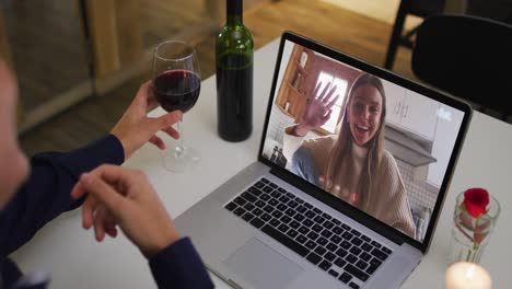 Mid-section-of-african-american-woman-holding-wine-glass-while-having-a-video-call-on-laptop-at-home