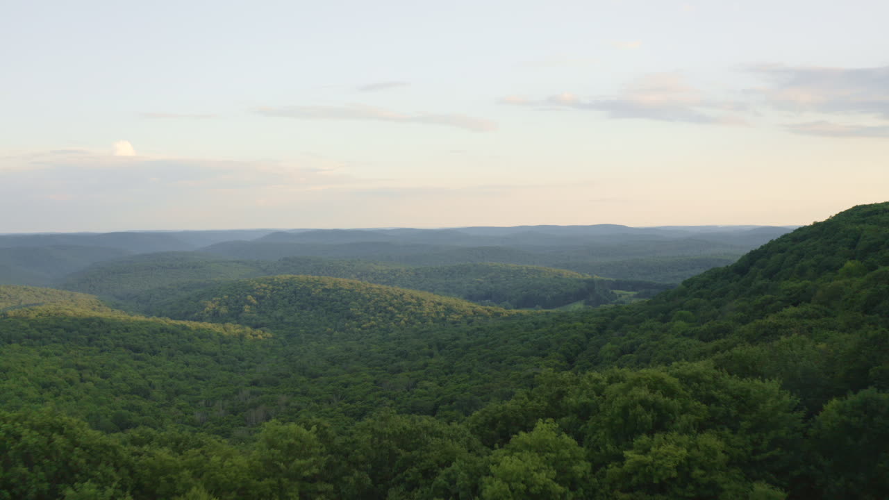 drone aéreo volando hacia adelante a través del bosque verde de verano y revelando un paisaje montañoso abierto al atardecer en pennsylvania