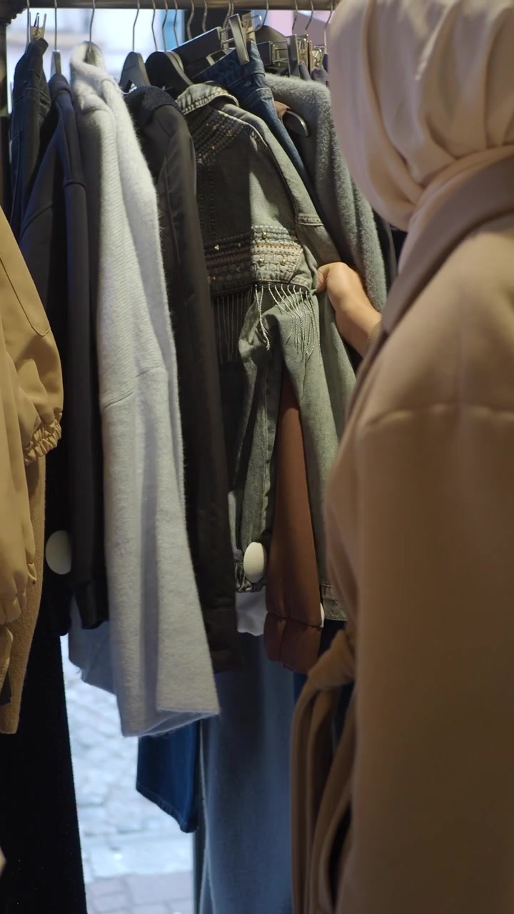 Nainen hijabissa selailee vaatteita vaaterekillä putiikissa.