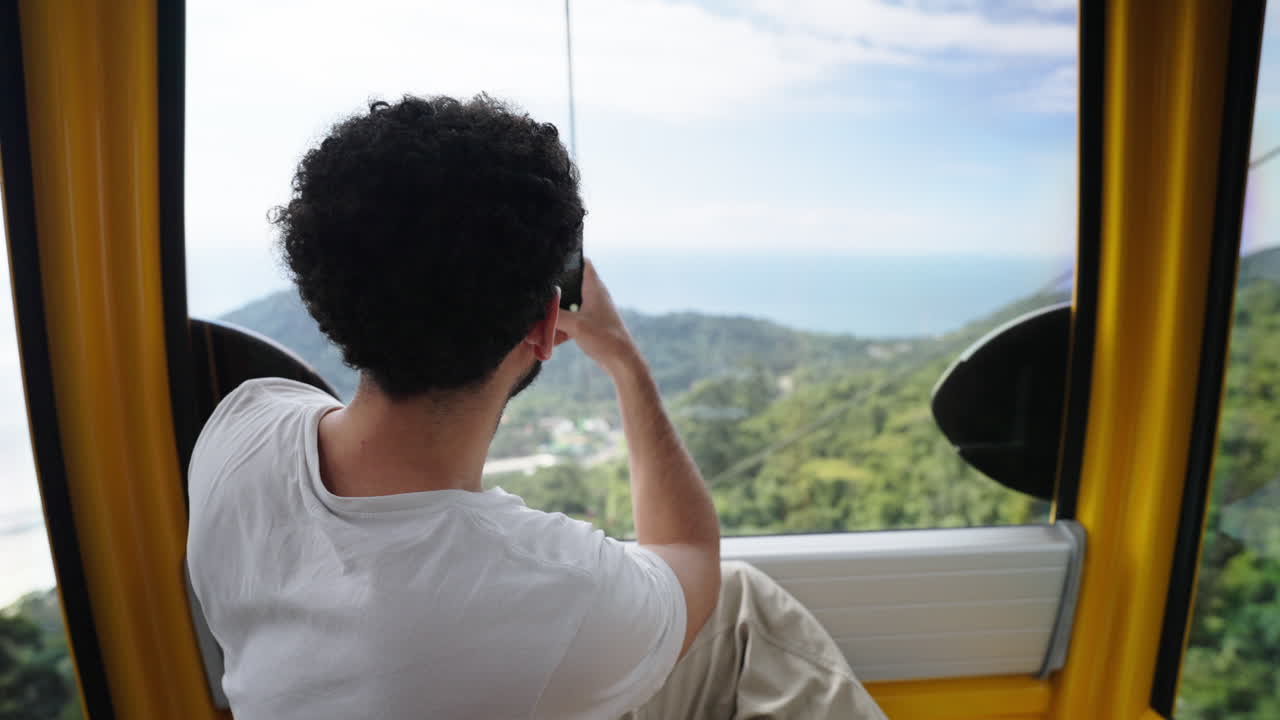 Man taking photo as tourist from inside moving cable car over forested hill environment, Balneário Camboriú, Santa Catarina, Brazil