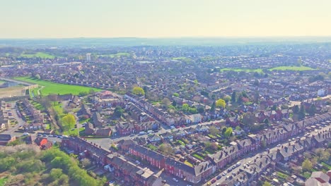 aerial view over the suburban residential area of wakefield, yorkshire, northern england, featuring redbrick houses, moving traffic, lush greenery, and a clear blue horizon.