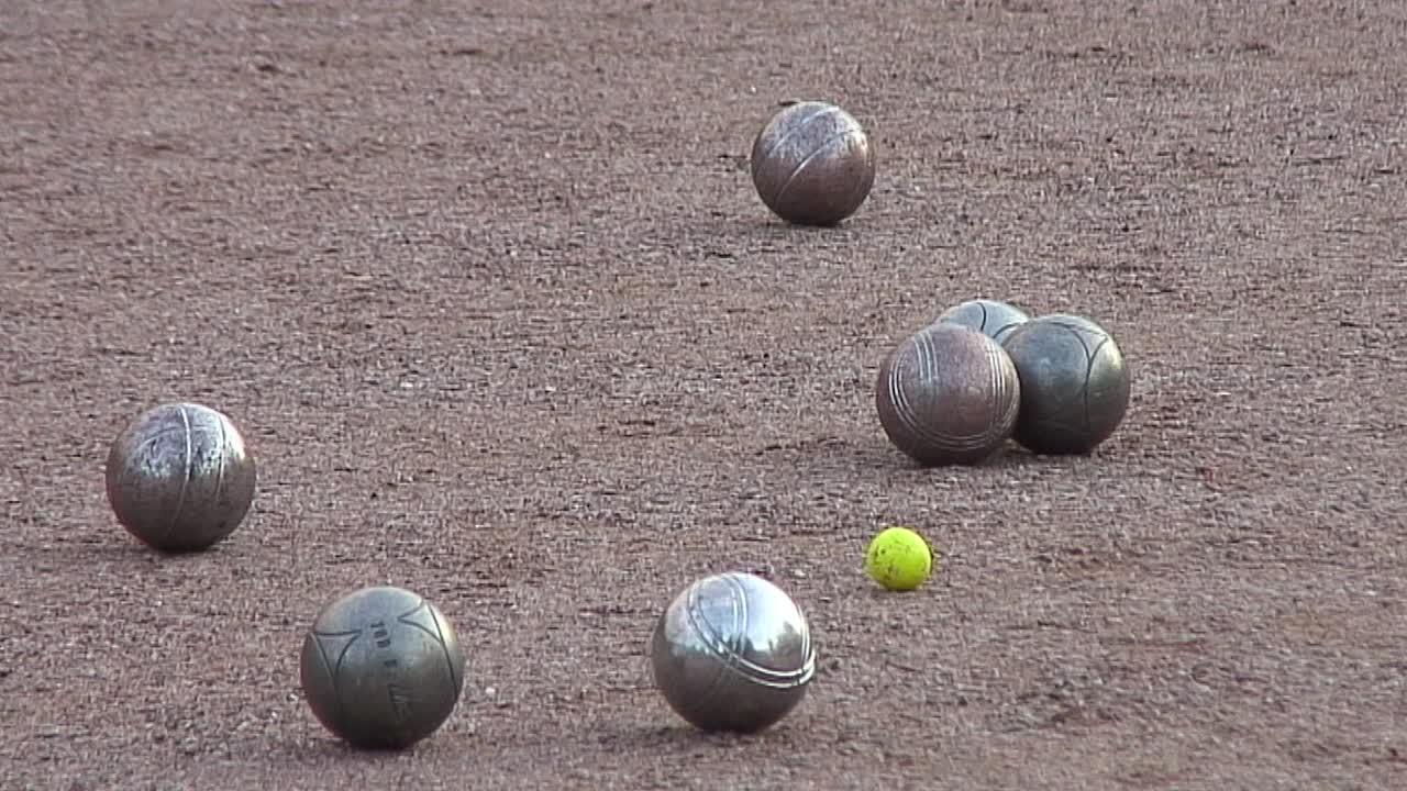 Steel boules thrown towards a yellow cocoon during a game of p&eacute;tanque between two teams