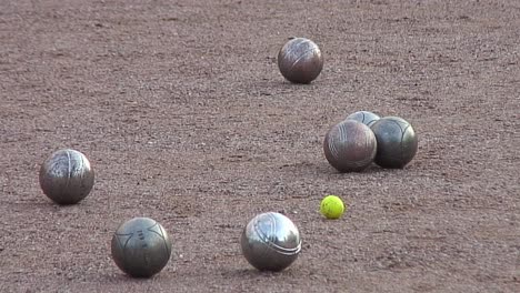 Steel-boules-thrown-towards-a-yellow-cocoon-during-a-game-of-pétanque-between-two-teams