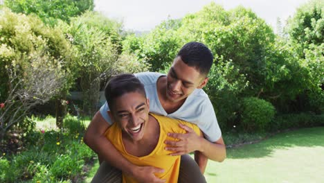 pareja de hombres gays de raza mixta sonrientes divirtiéndose a hombros en el jardín