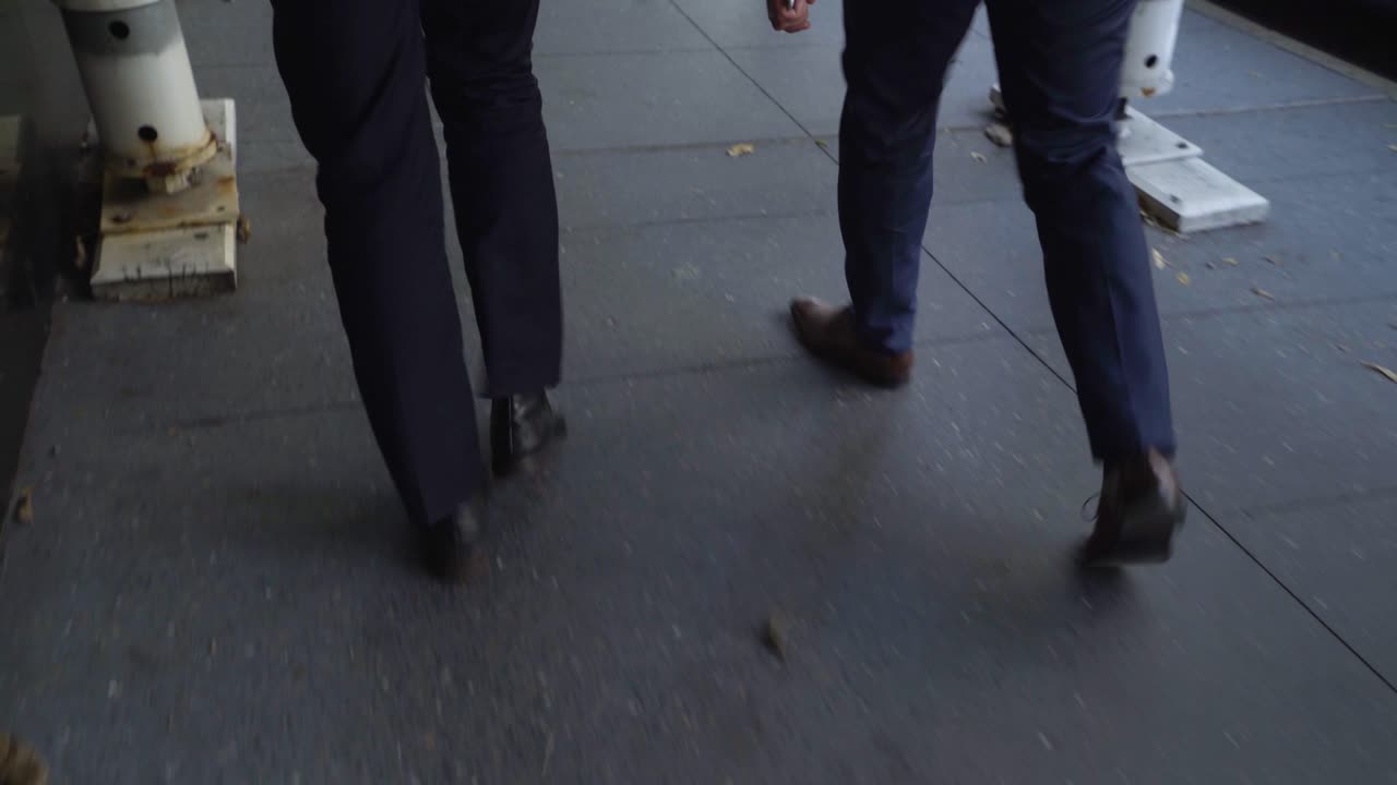 Inquadratura dalla vita in giù di due uomini in abito che camminano per una strada cittadina