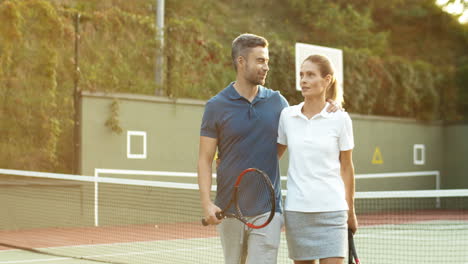 Glückliches-Paar,-Das-Den-Tennisplatz-Im-Sonnenlicht-Des-Sonnenuntergangs-Umarmt-Und-Verlässt-1