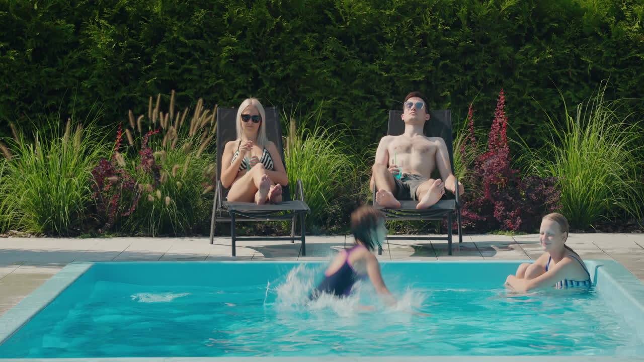 Familien slapper af ved deres pool i husets baghave. Voksne solbader på liggestole, to børn svømmer i poolen.