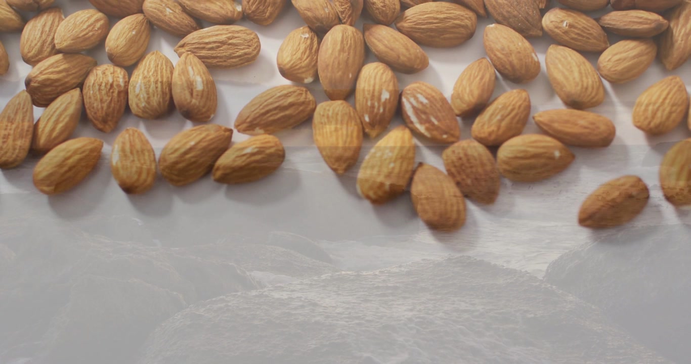 Amandes glissant du haut, s'étalant sur un plateau lumineux et recouvrant un paysage marin pour symboliser l'abondance.