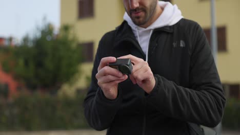 Hombre-Con-Barba-Y-Gorra-Cambiando-La-Configuración-De-La-Pantalla-Táctil-De-La-Cámara-Dji-Osmo-Action-4-Al-Aire-Libre