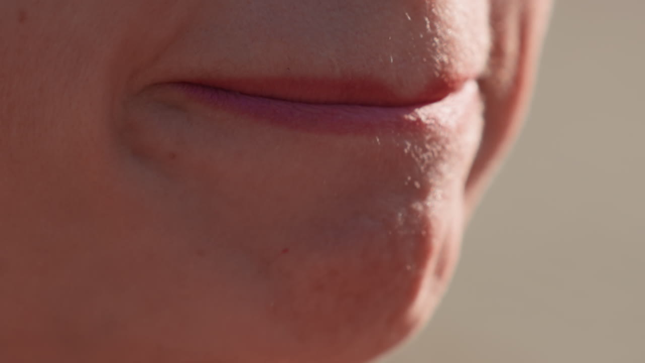 Primo piano estremo di una donna che applica il rossetto sulle labbra all'aperto alla luce naturale del sole, evidenziando i dettagli dell'applicazione del cosmetico, la bellezza femminile, la cura della pelle e la cura di sé con una nitida messa a fuoco cinematografica