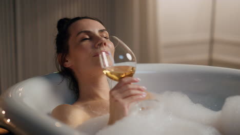 serene girl sipping alcohol at spa room closeup. relaxed woman taking foam bath