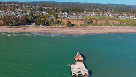 Storm-damaged-remains-of-Seacliff-pier-sunken-under-California-Pacific-ocean-shoreline,-Orbiting-aerial-view