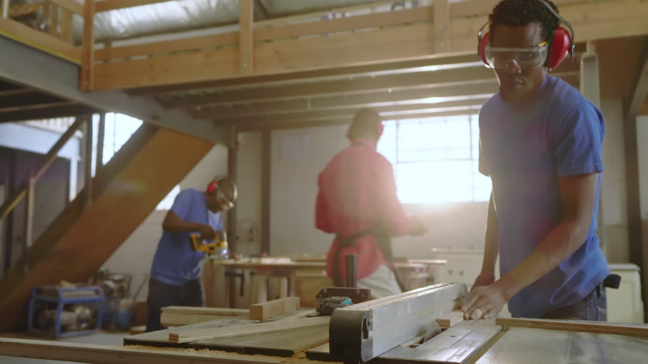 Approaching table saw, African American craftsmen cutting and trimming planks in shop, copy space