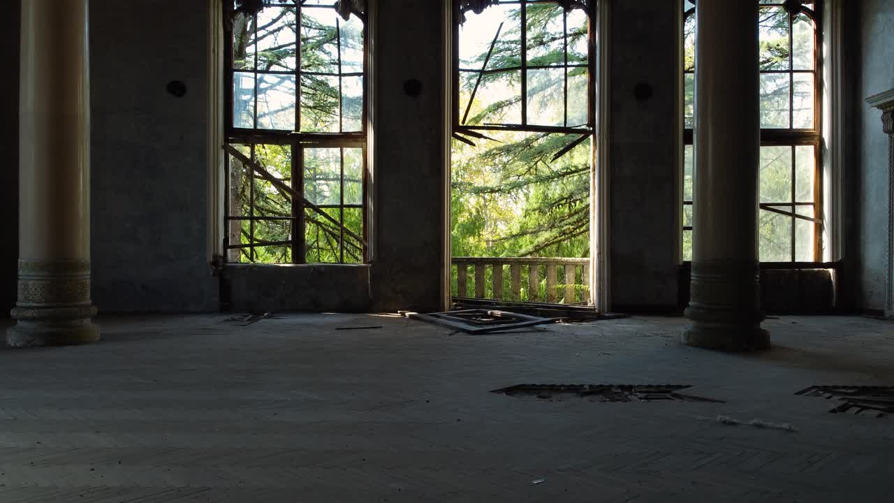 Broken windows and overgrown trees seen from inside abandoned sanatorium in Tskaltubo