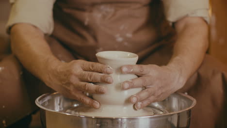 pottery artist shaping a clay vessel on a potters wheel
