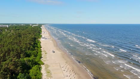 aerial view of jurmala beach, latvia, with pine forest on the left and calm waves of the baltic sea on the right, captured during a drone pull out showing the expansive coastline and beachgoers