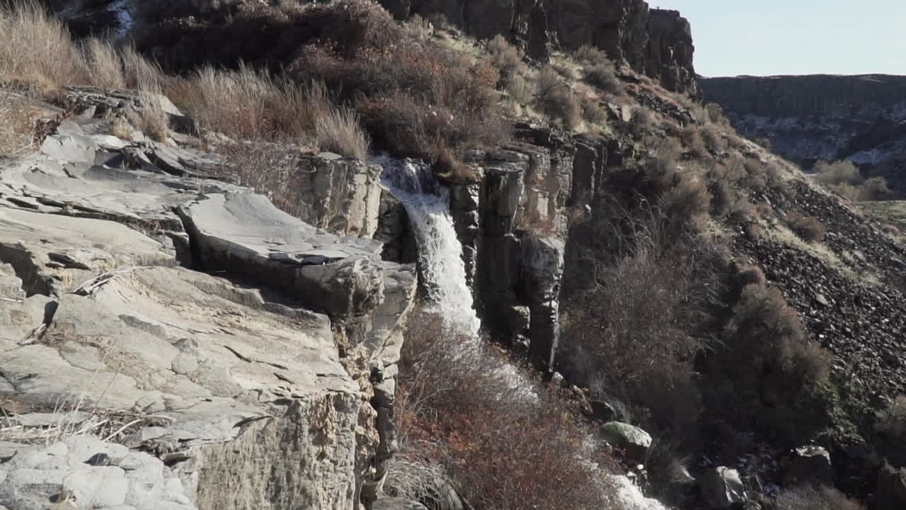 wide shot of a waterfall, surrounded by shrubs, bushes and rocks