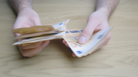 nervous, stressed male hands counting his paper money bills on a wooden table