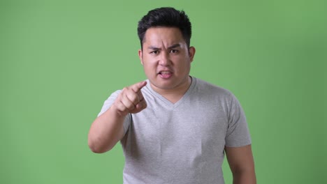 young handsome overweight asian man against green background