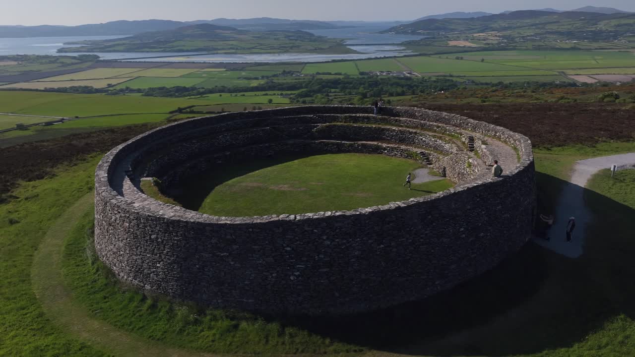 Grianan of Aileach, County Donegal, Ireland, June 2023. Drone close-up counter clockwise orbit as people explore the stone hillfort with Lough Swilly and Derry City Northern Ireland in the distance.