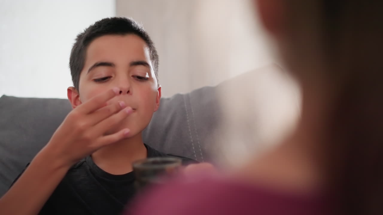 약 복용하는 어린 소년을 지켜보며 건강을 확인하고, 걱정하는 마음으로 치료를 돕고 약을 투여하며 건강을 지원하는 사람의 뒷모습 클로즈업