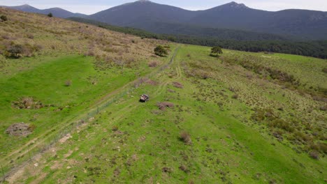 Cinematic-aerial-shot-4x4-car-driving-on-green-hills-during-sunny-summer-day---Adventure-trip-expedition-in-Spain