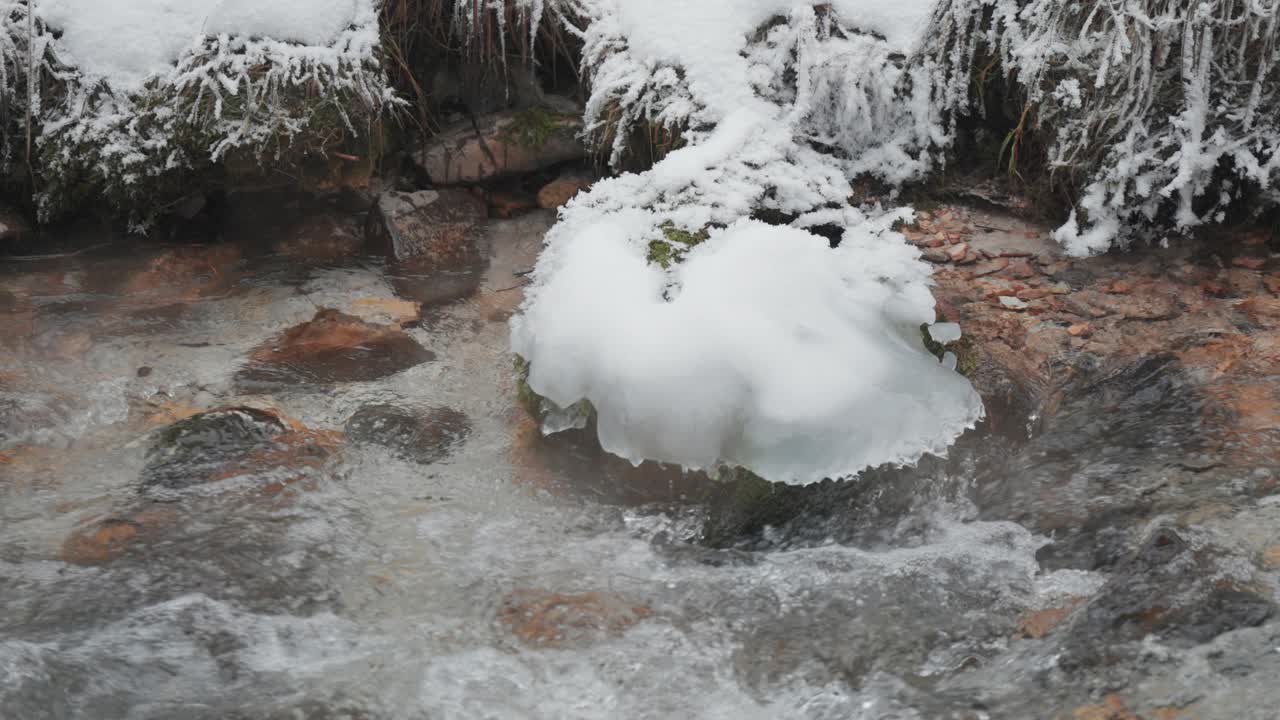 A shallow mountain stream flows through the frozen landscape. Grass and stones are covered with ice and hoarfrost.
