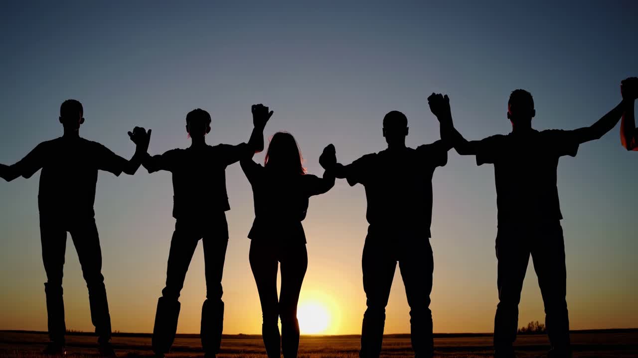 Silhouetted group holding hands at sunset, symbolizing unity. Captured from a low angle