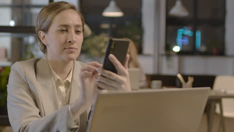 mujer de negocios sonriente enviando mensajes de texto por teléfono móvil mientras trabaja en la oficina