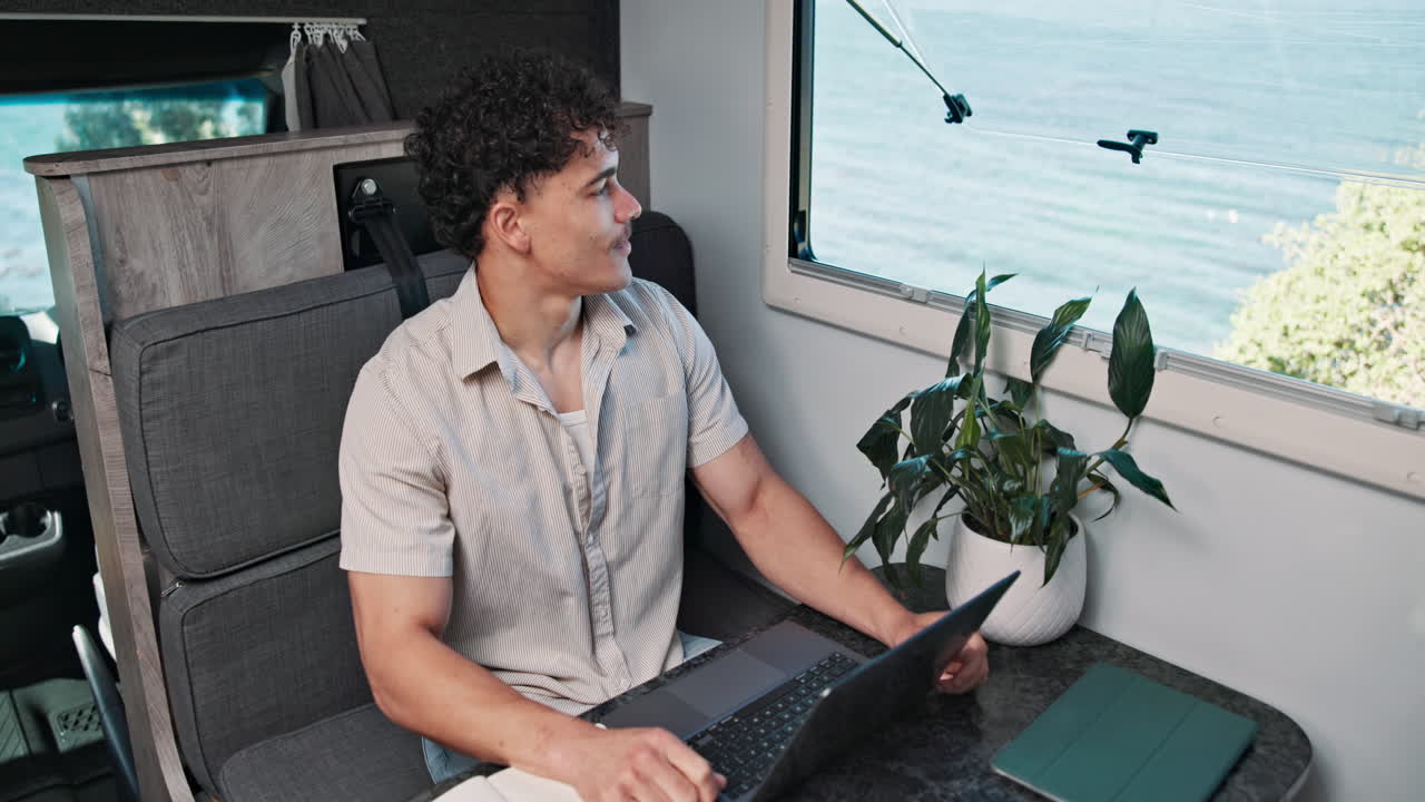Young Man Working on Laptop in Camper Van with Ocean View