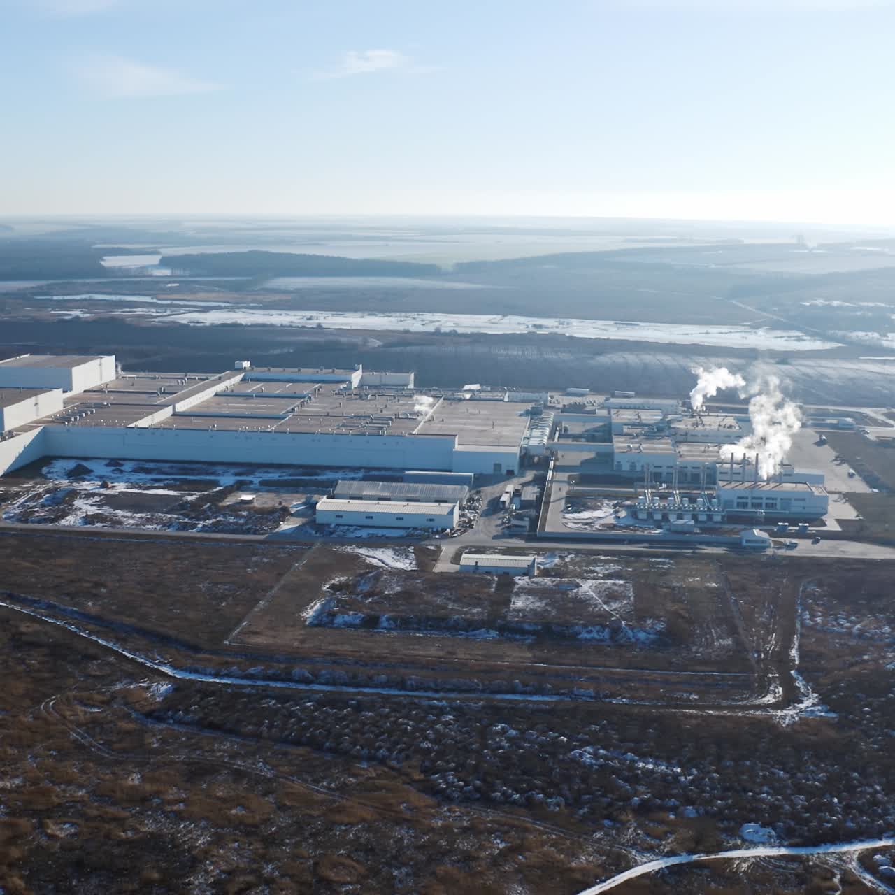 Big territory of industrial factory surrounded by nature. View from above on the roofs of a modern plant in the countryside in winter. Aerial view.