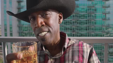 portrait shot of black man with cowboy hat tipping shot glass