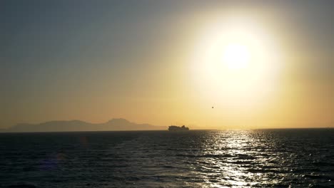 Vista-Del-Horizonte-Y-Un-Ferry-De-Vela-En-Las-Aguas-Griegas-Del-Mar-Jónico,-Todo-Bajo-Los-Rayos-Del-Sol-Poniente.