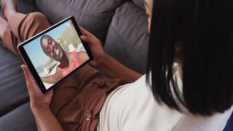 mujer afroamericana haciendo una videollamada en una tableta digital sentada en el sofá en casa