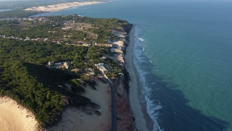 Extreme-wide-tilt-up-aerial-drone-shot-revealing-the-stunning-Cliffs-of-Cacimbinhas-in-Pipa,-Brazil-Rio-Grande-do-Norte-with-tourists-sand-boarding,-paragliders-flying-around,-and-small-waves