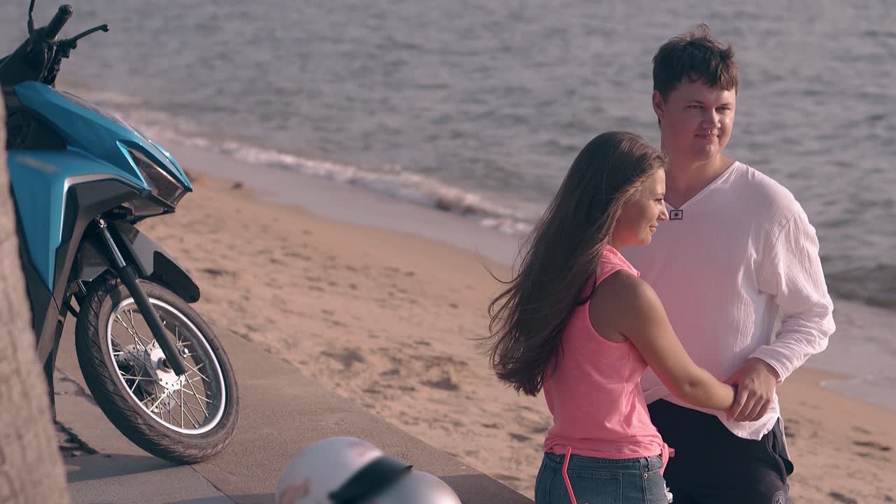 밝은 분홍색 을 입은 여자가 파란 바다에 맞서 키가 큰 남자를 키스합니다.