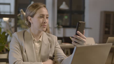 mujer de negocios sonriente que tiene una videollamada con el teléfono móvil mientras trabaja en la oficina 1