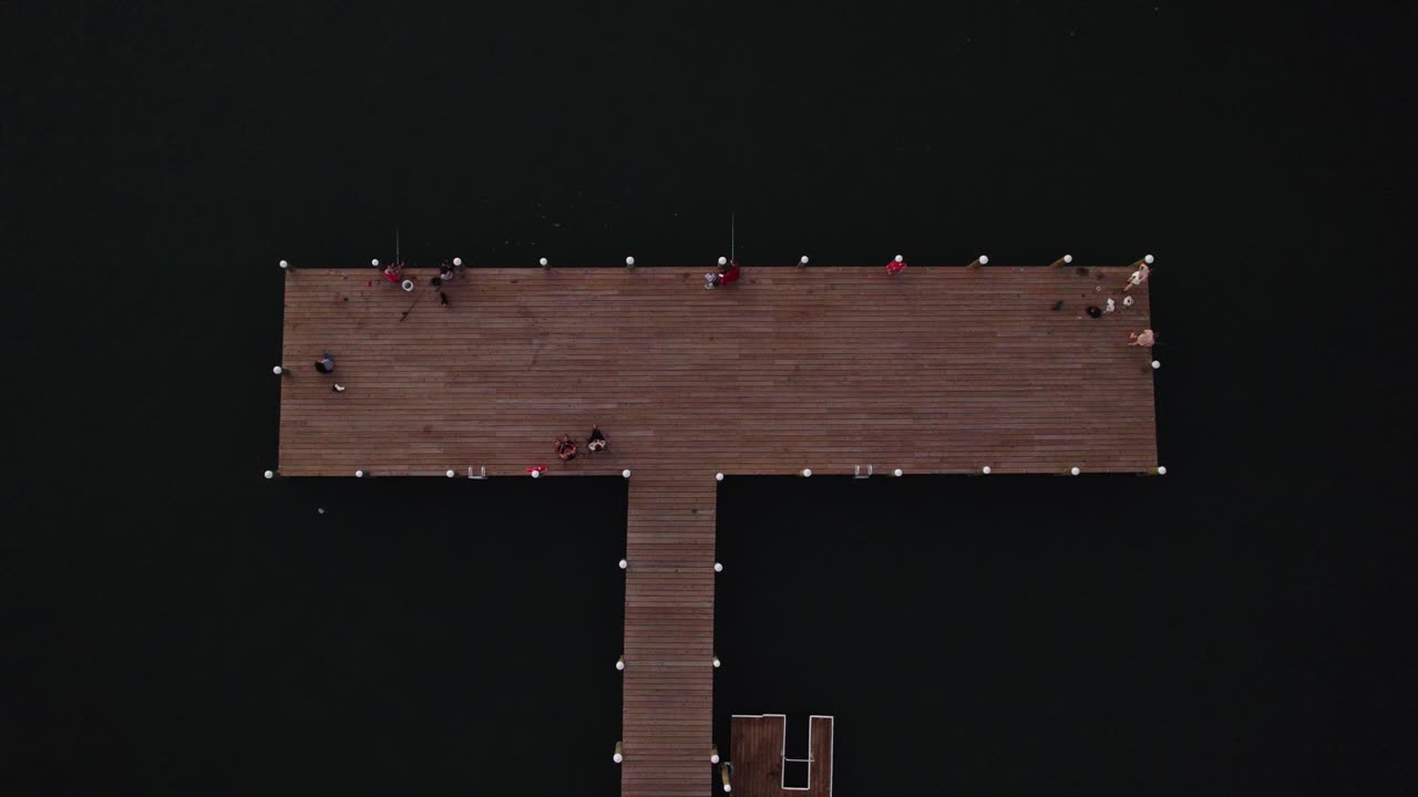 Drone top down descend on wooden T shaped pier dock with fishermen on edges