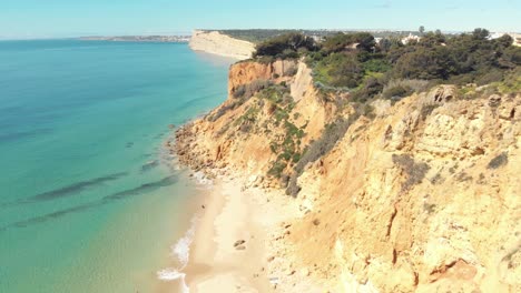 Golden-sandy-beach-and-yellow-limestone-scarps-of-Lagos,-Algarve-Coast,-Portugal---Aerial-fly-over-tracking-shot