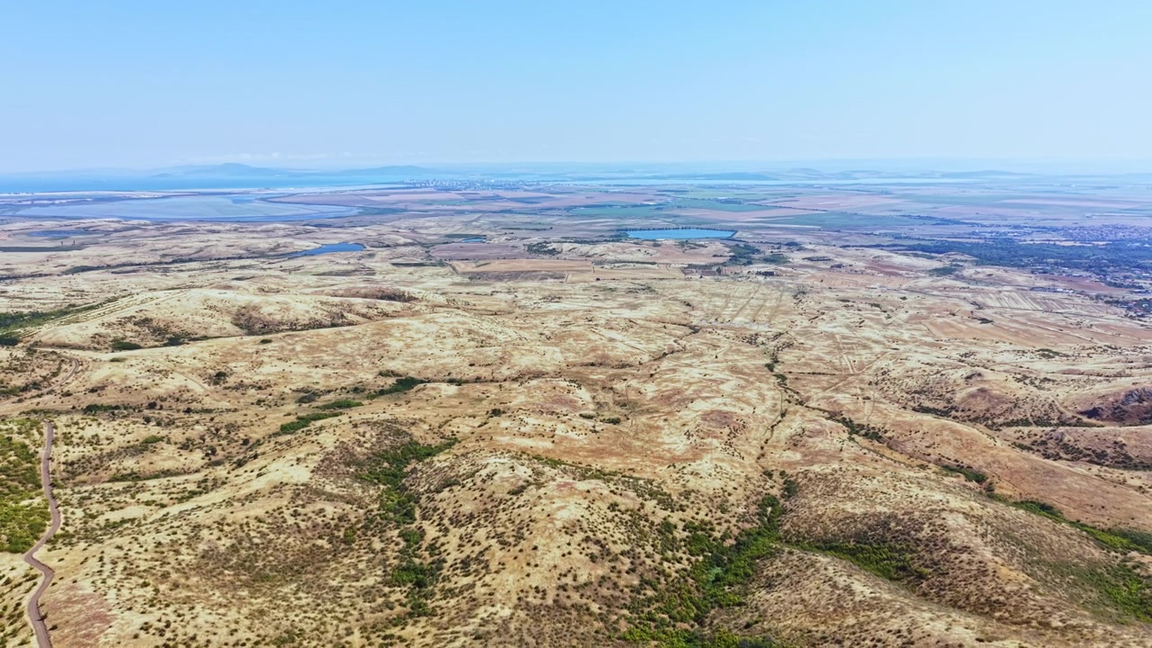 Ampia vista di un paesaggio arido con colline, specchi d'acqua e montagne distanti in una giornata limpida e soleggiata in un'area aperta.