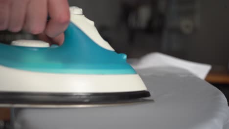 Young-man-irons-white-shirt-on-ironing-board:-Perspective-close-up