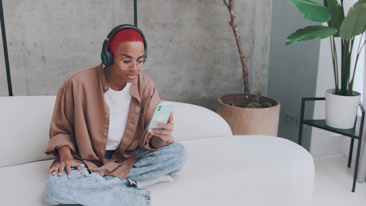 Young cheerful african american woman with mobile phone sits at sofa