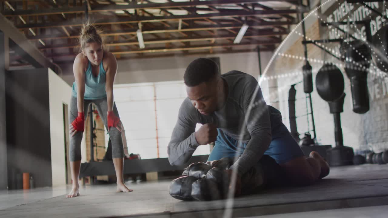 Male trainer adjusting heavy bag, teaching woman short punches, particle waveforms accenting boxing