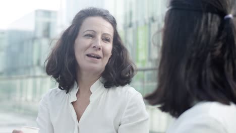 Fröhliche-Bürofreundinnen-Sitzen-Draußen,-Trinken-Kaffee,-Reden-Und-Lachen-1