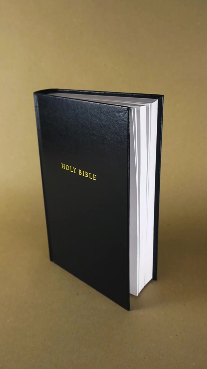 Sacra Bibbia con copertina in pelle nera e eleganti scritte dorate, che scivola dolcemente su uno sfondo neutro marrone chiaro. Testo religioso cristiano che simboleggia fede e spiritualità