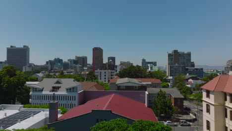 Vuelo-Bajo-Por-Encima-De-Edificios-Y-árboles-En-El-Distrito-Urbano.-Oficinas-De-Varios-Pisos-O-Casas-De-Apartamentos-Contra-El-Cielo-Azul-Claro.-Ciudad-Del-Cabo,-Sudáfrica