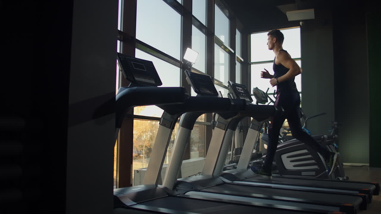 Young athletic men and women exercising and running on treadmill in sport gym. Slow motion Near a large panoramic window