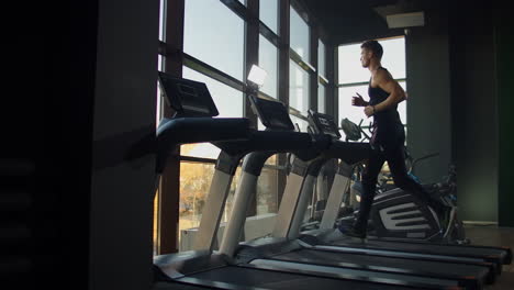 Jóvenes-Atléticos,-Hombres-Y-Mujeres,-Haciendo-Ejercicio-Y-Corriendo-En-Cinta-En-Un-Gimnasio-Deportivo.-Cámara-Lenta-Cerca-De-Una-Gran-Ventana-Panorámica