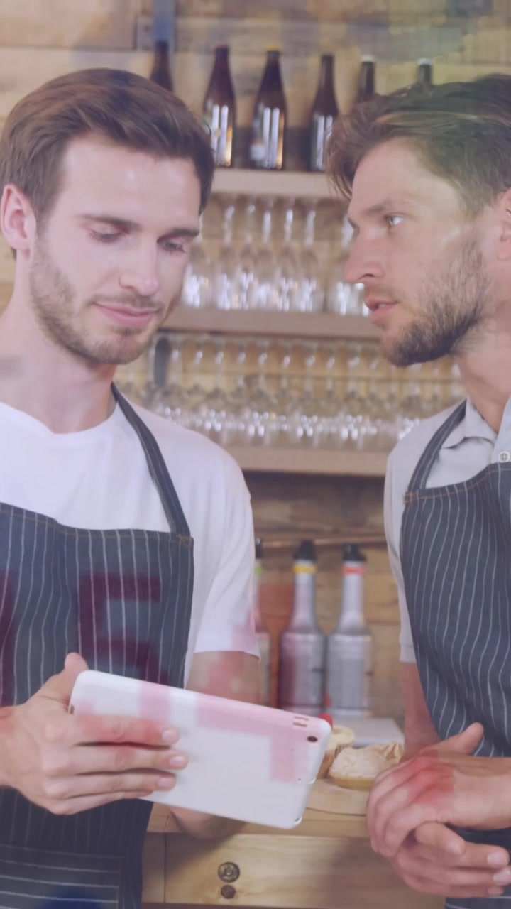 Animation von Währungssymbolen und Zahlen, kaukasische männliche Kollegen diskutieren über einem Tablet in einem Café