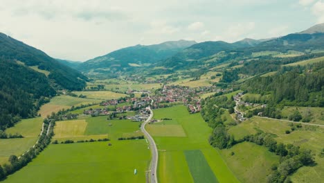 sweeping drone view of st. peter am kammersberg nestled in a lush alpine valley, surrounded by dense forests and dramatic mountain peaks